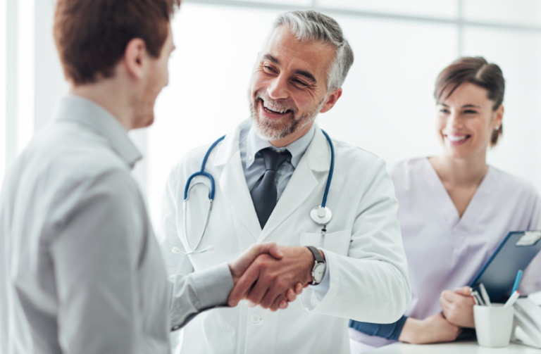 médico apertando a mão de um homem com uma enfermeira ao fundo da imagem