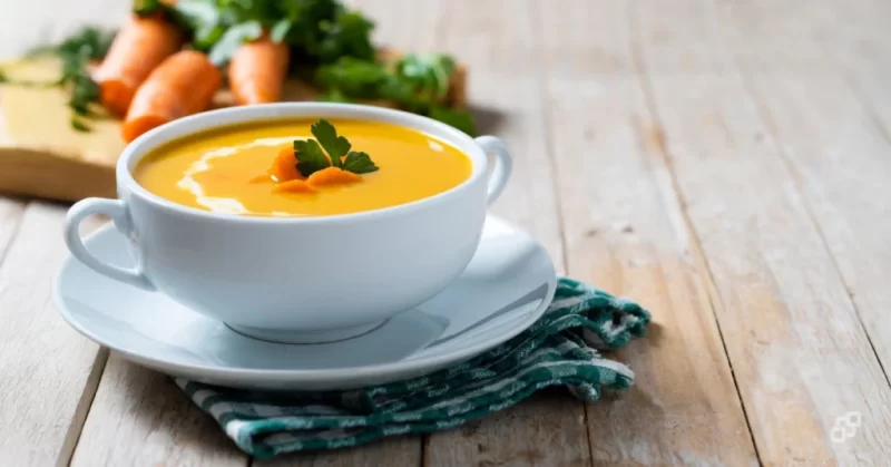 Tigela de creme de cenoura com leite de coco sobre mesa de madeira, opção de refeição cremosa para pacientes em tratamento do câncer